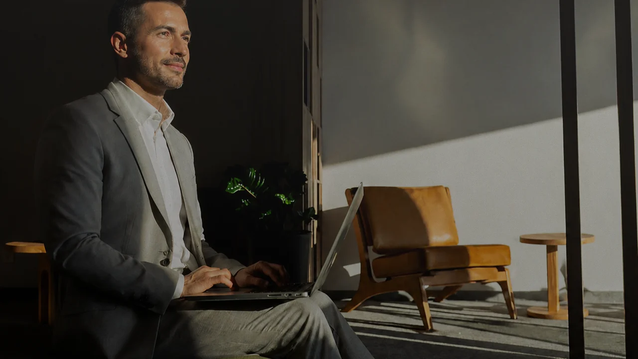 Man in a grey blazer working on a laptop in a lounge